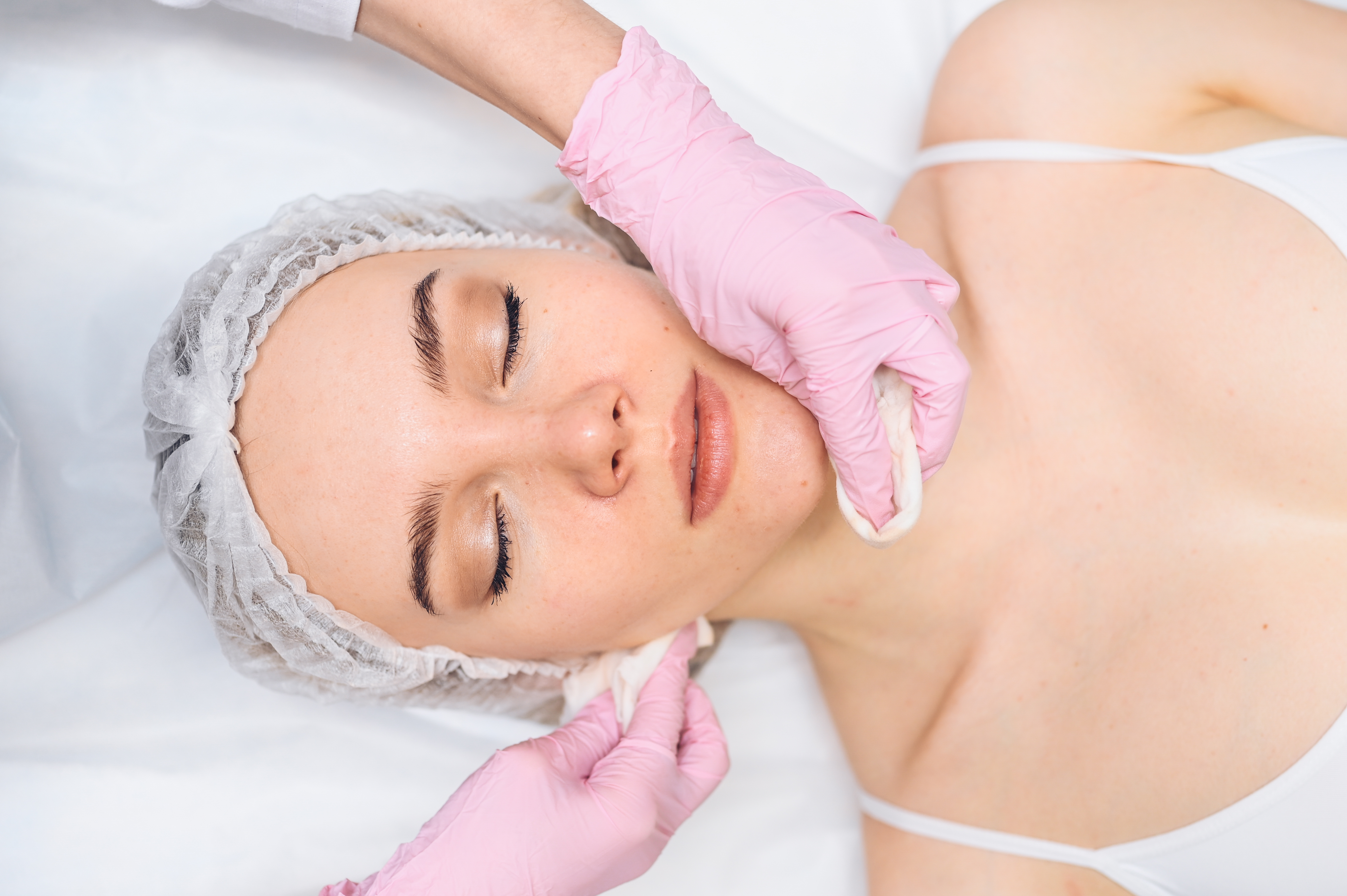 Косметолог удаляет декоративную косметику и поверхностные загрязнения с помощью очищающих средств по типу кожи: молочка, геля или пенки